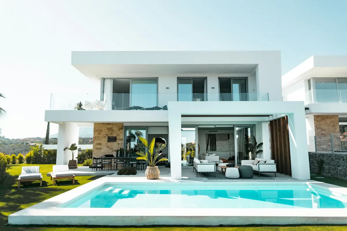 Swimming pool facing a white house and outdoor seating